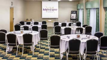 Ein Konferenzraum mit runden Tischen, Stühlen und einer Präsentationsleinwand, auf der 'Mercure Hotels' angezeigt wird.