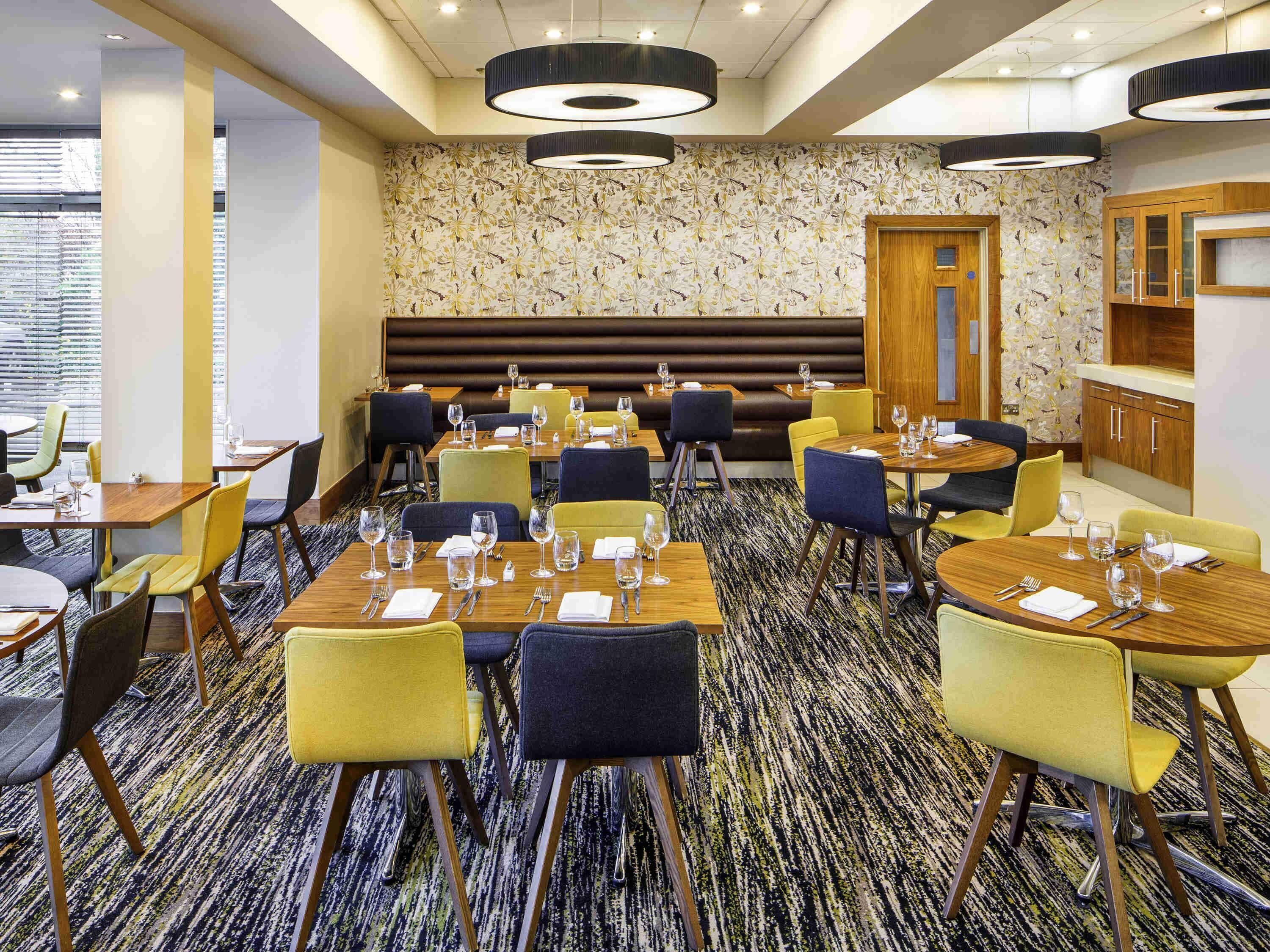 A restaurant with multiple tables and chairs, a patterned carpet, and a wooden bench area.