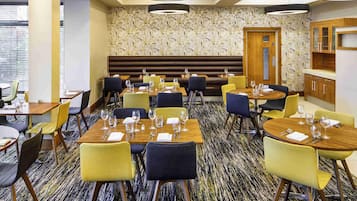 A restaurant with multiple tables and chairs, a patterned carpet, and a wooden bench area.