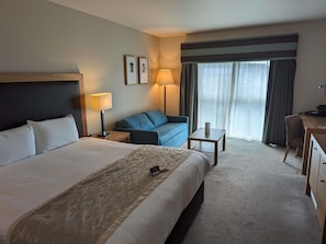 A hotel room with a bed, a desk, a chair, a sofa, a lamp, and a window with curtains.