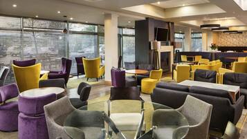 Un hall d’hôtel moderne offrant différents types de sièges, notamment des tables rondes et des canapés, ainsi qu’une cheminée.