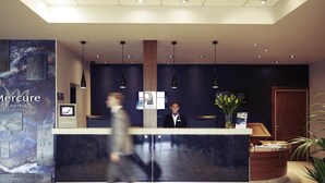 A hotel reception desk with a modern design, a receptionist, and a large artwork on the wall.