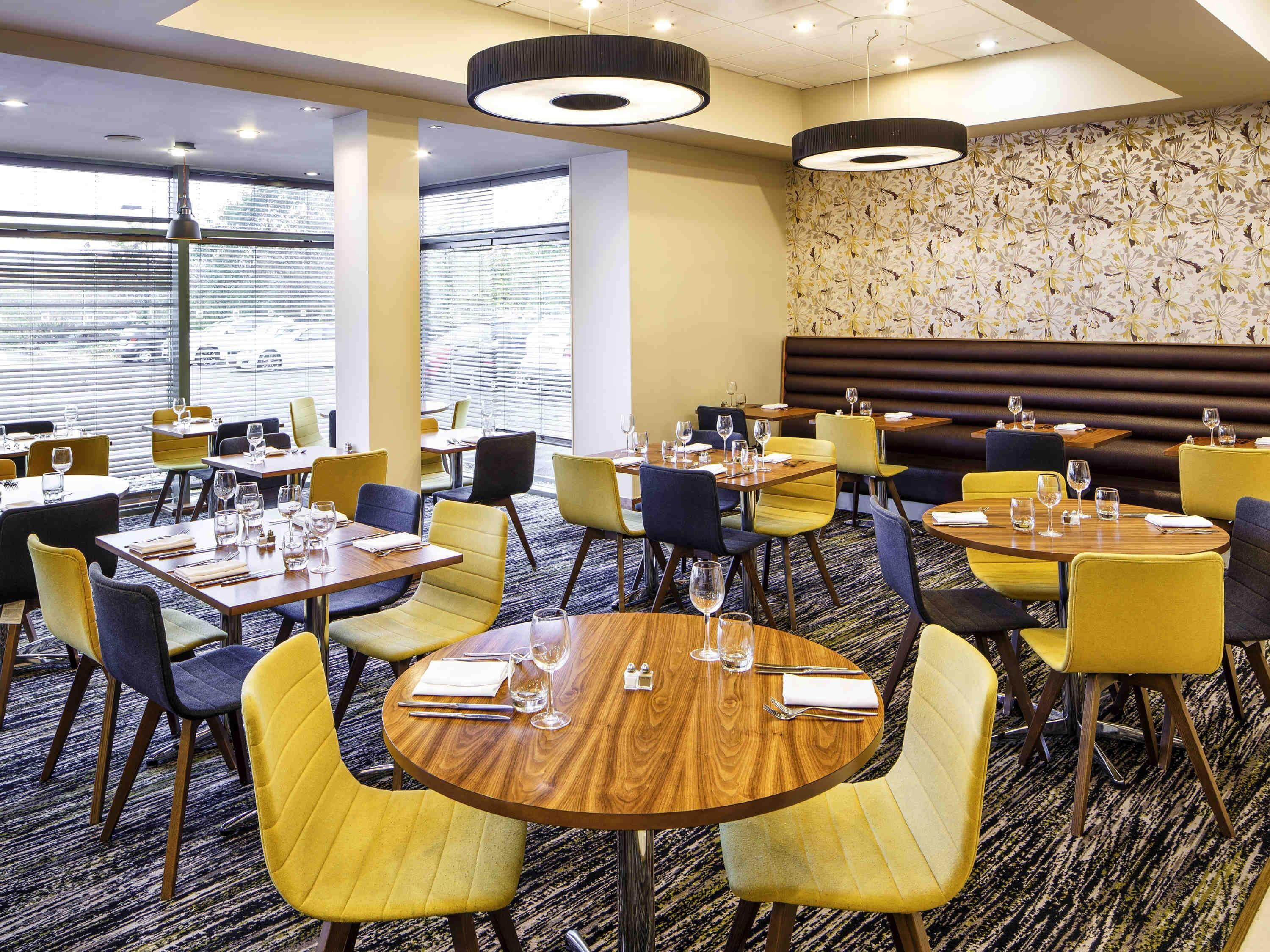A hotel dining area with round tables, yellow chairs, and a patterned wall.