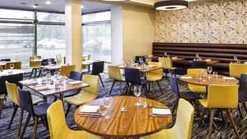 A hotel dining area with round tables, yellow chairs, and a patterned wall.