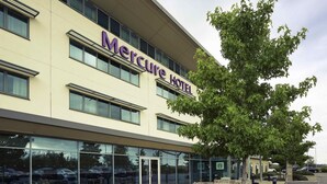 The exterior of the Mercure Hotel with a clear view of the entrance, outdoor seating area, and surrounding greenery.