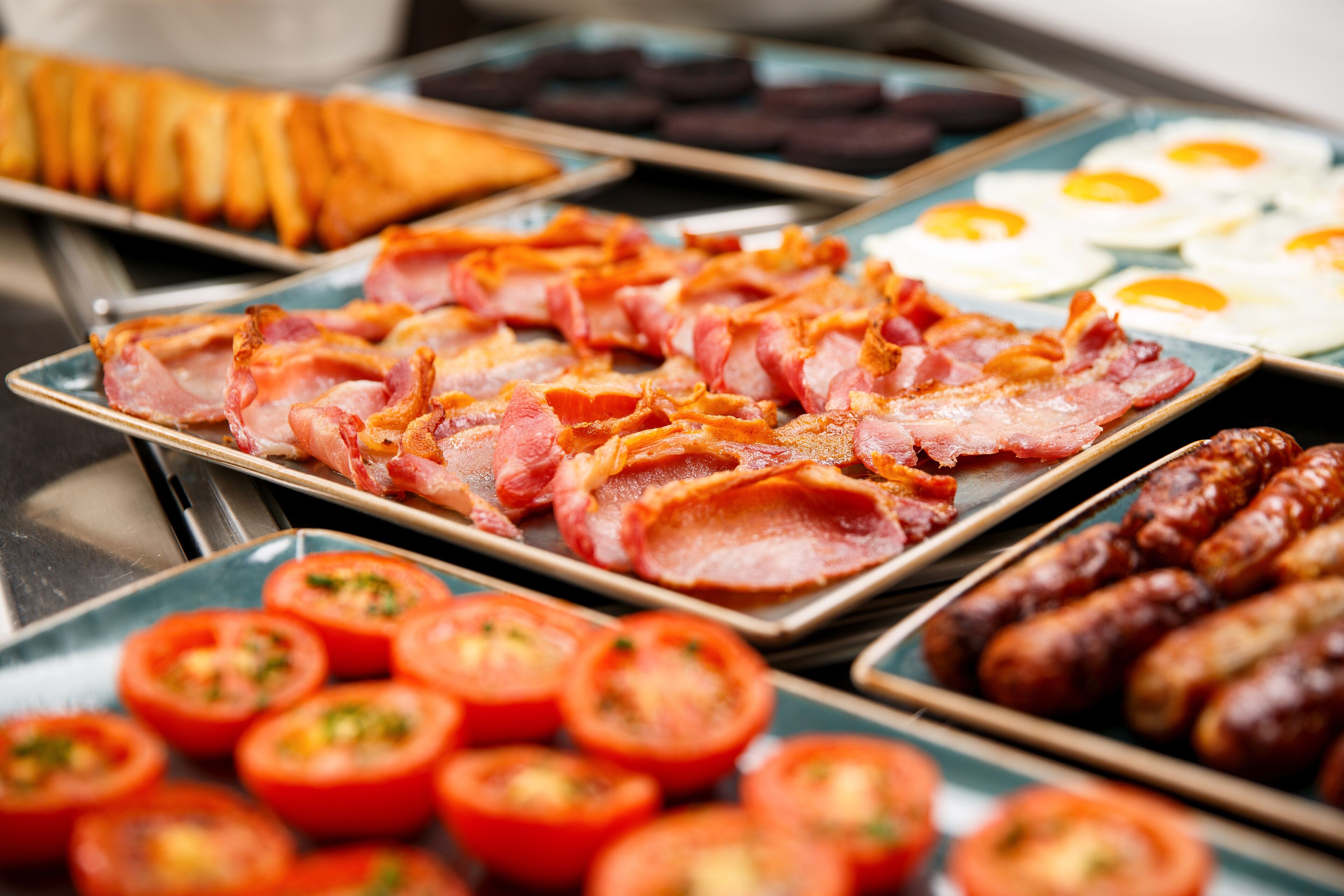 Ein Frühstücksbuffet mit Speck, Würstchen, Eiern und Tomaten.