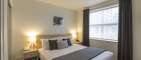 A hotel room with a large bed, two bedside lamps, a nightstand, a window with curtains, and a framed picture on the wall.