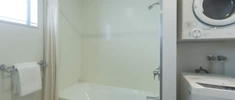A bathroom with a glass-enclosed shower, a white bathtub, and a front-loading washing machine.