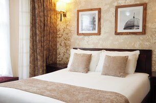 Habitación de hotel con una cama grande, dos almohadas, cabecero y dos cuadros en la pared.