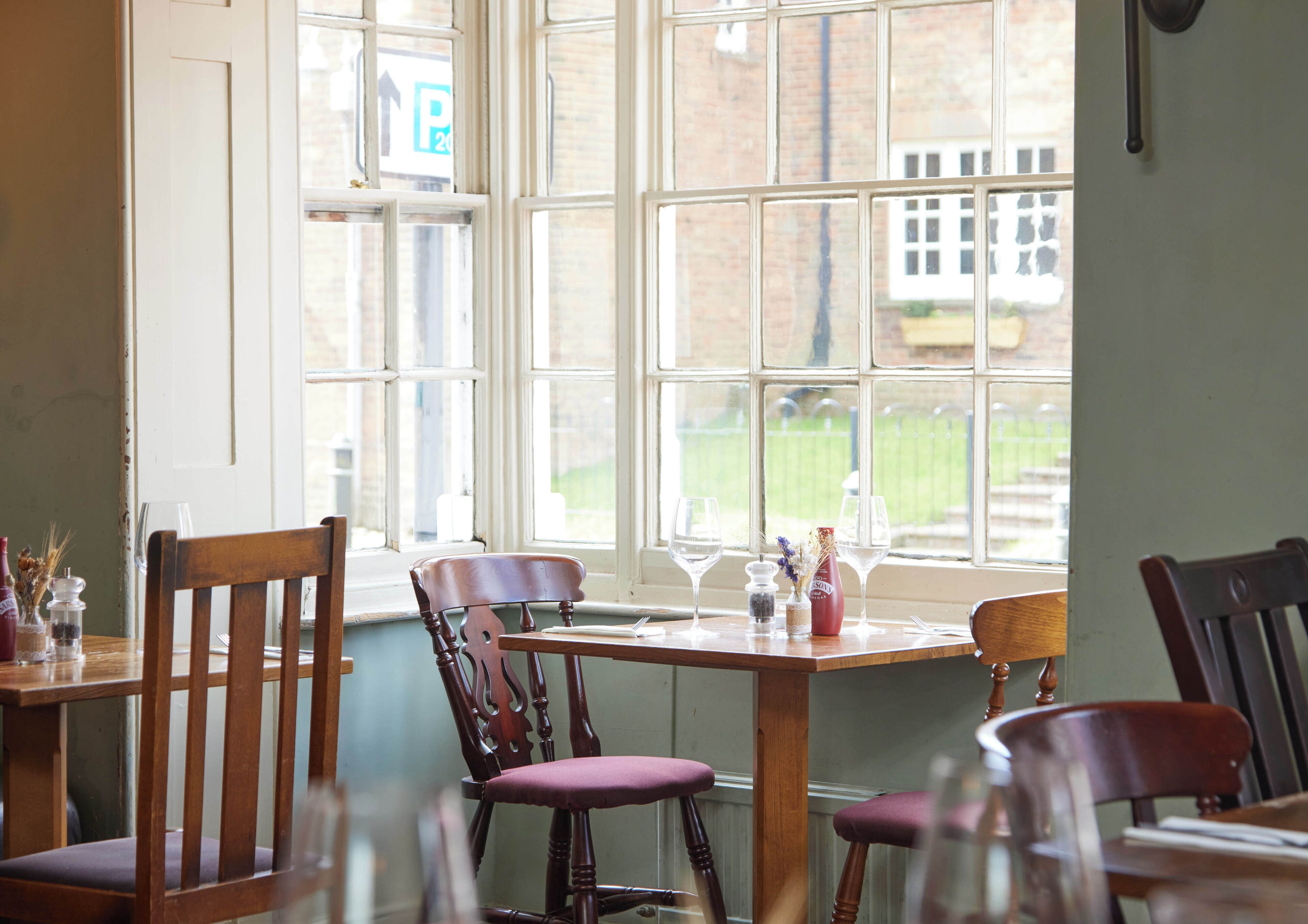 A dining area with wooden chairs and tables, large windows, and a view of a building and greenery outside.