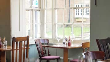 A dining area with wooden chairs and tables, large windows, and a view of a building and greenery outside.