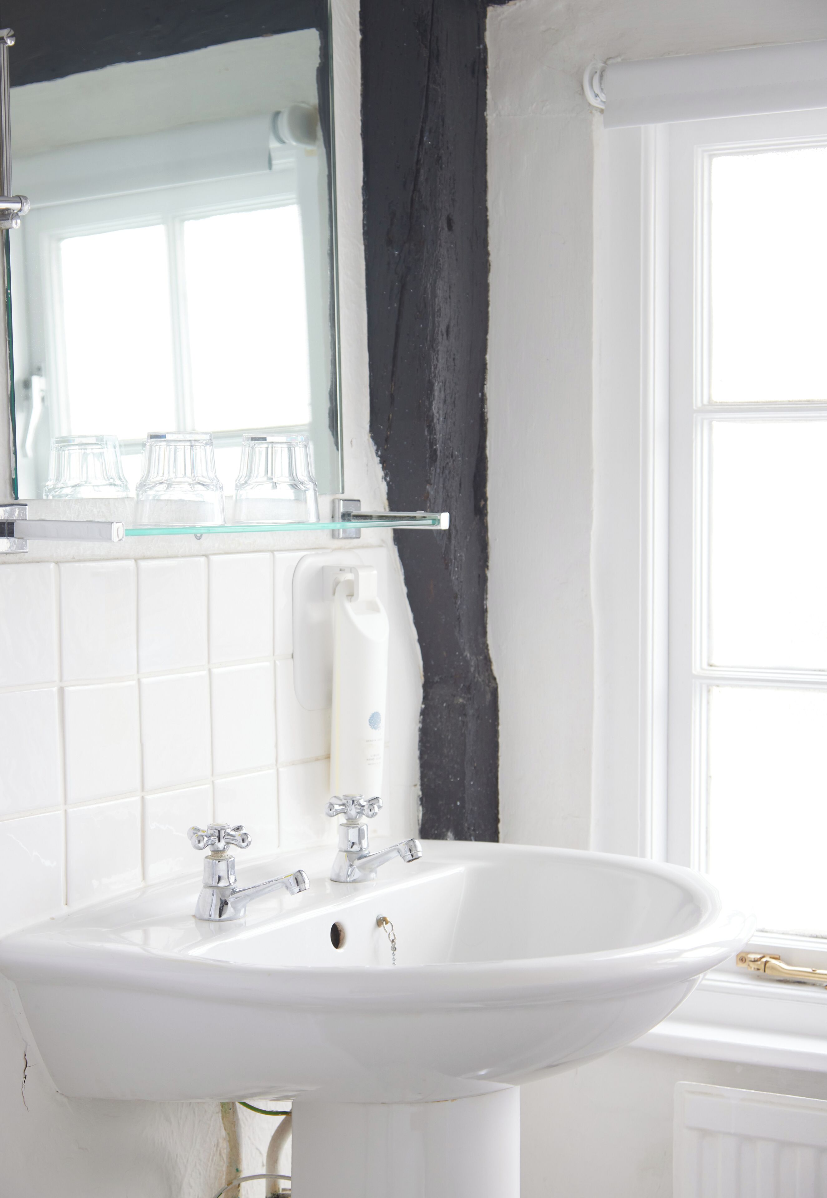 A bathroom with a white sink, a glass shelf with three glasses, and a large mirror above the sink.