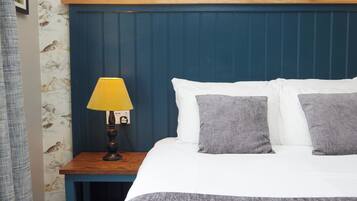 Ein Schlafzimmer mit einem blauen Kopfteil, einem Nachttisch aus Holz mit einer gelben Lampe sowie einem Bett mit weißer und grauer Bettwäsche.