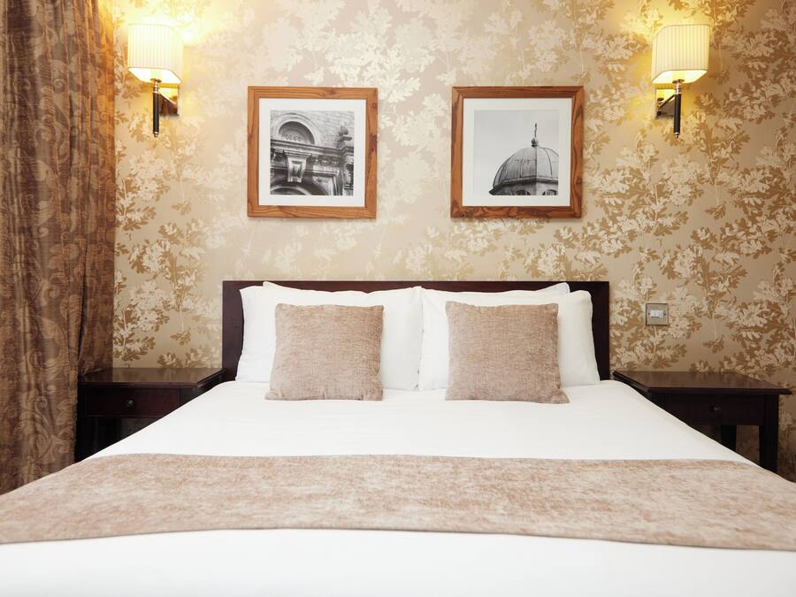 A neatly made bed with a white and beige bedspread, two pillows, and a brown throw blanket. There are two framed pictures on the wall above the bed.