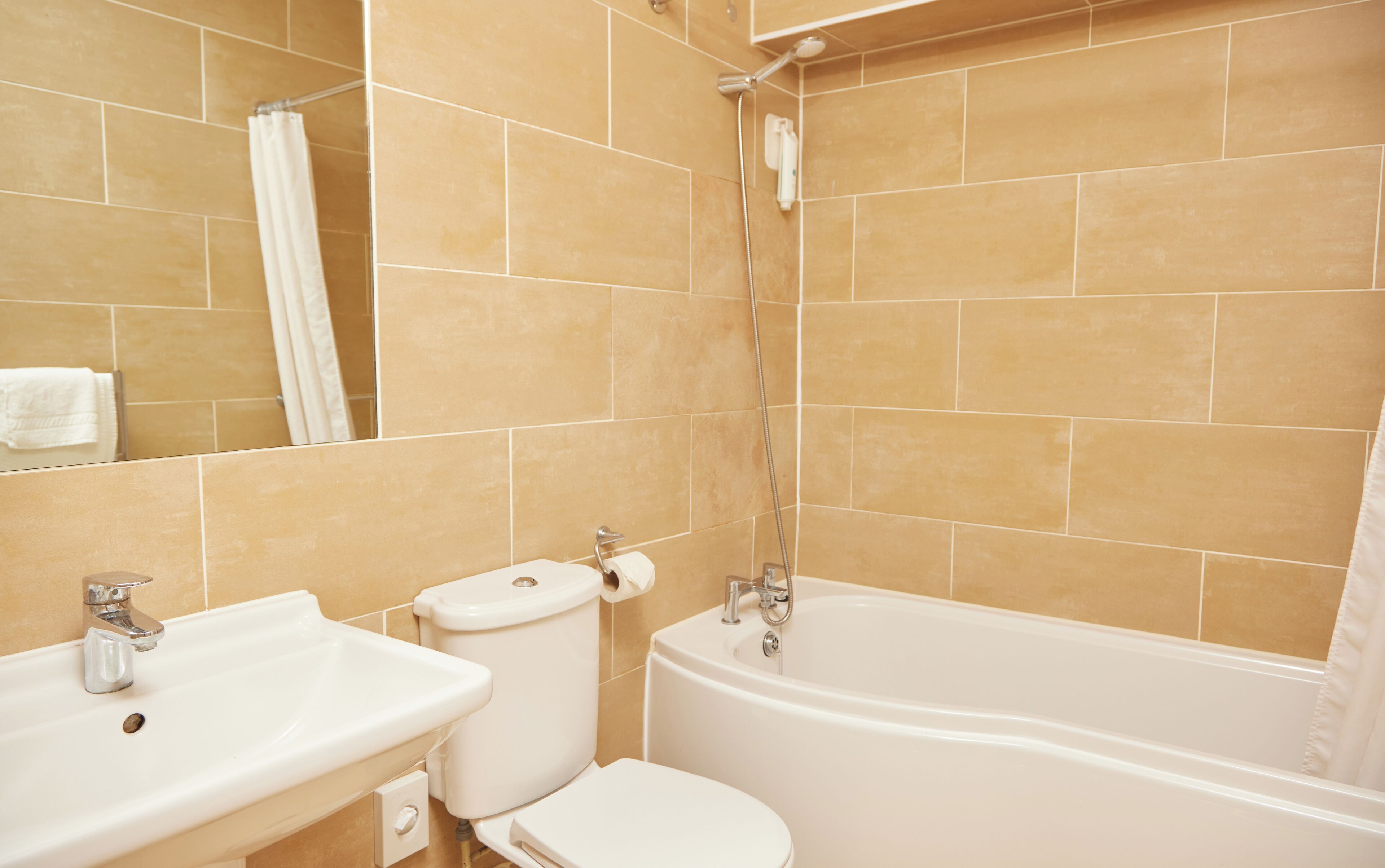 Un baño con azulejos color beige, un lavamanos, inodoro y bañera.