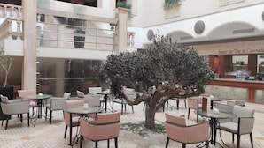 Ein großzügiger Innenbereich mit verschiedenen Sitzgelegenheiten, einem zentralen Baum und einer sichtbaren Treppe, die zu einer oberen Ebene führt.