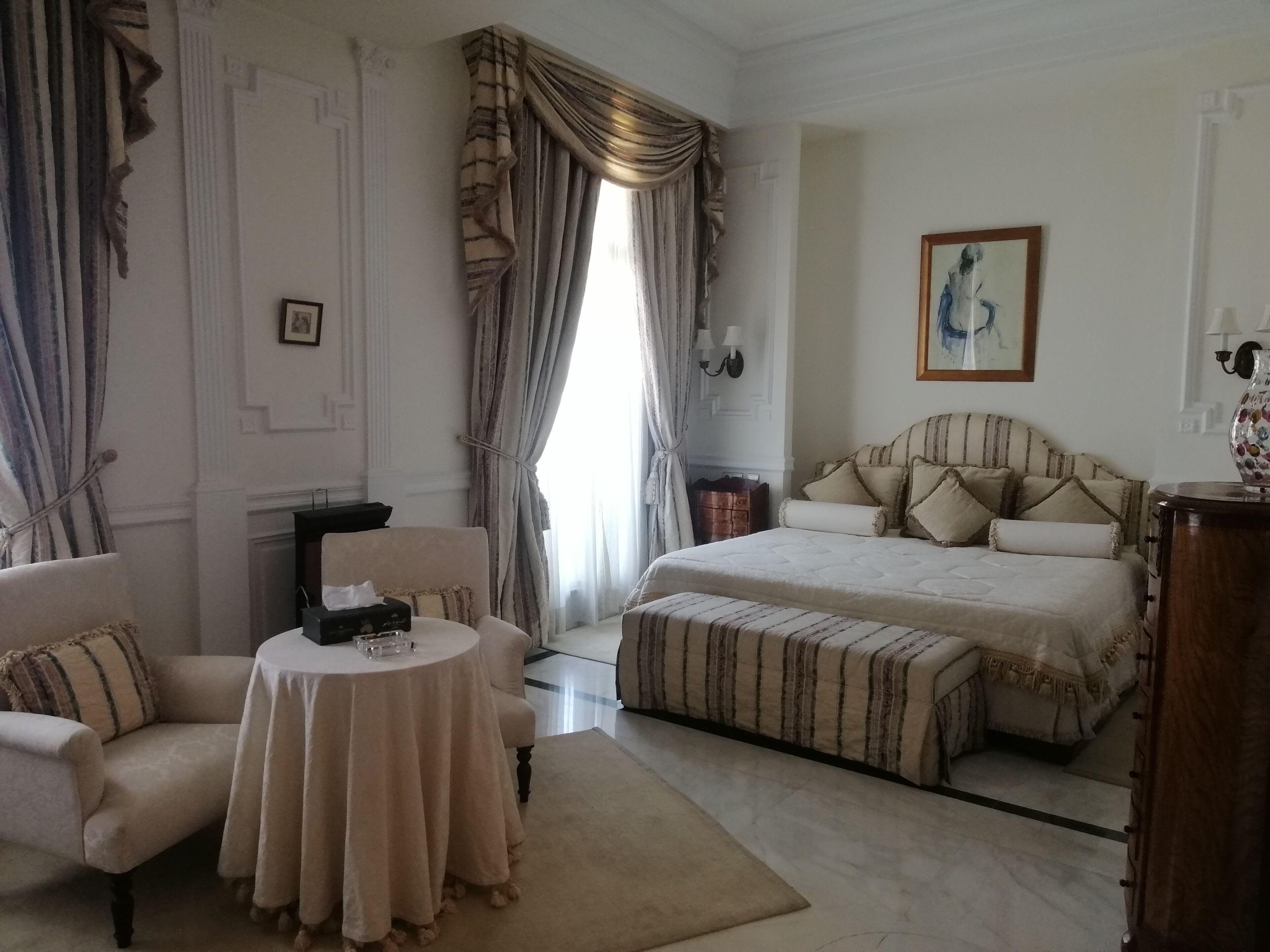 A hotel room with a large bed, a sitting area with a table, and a view of the outdoors.