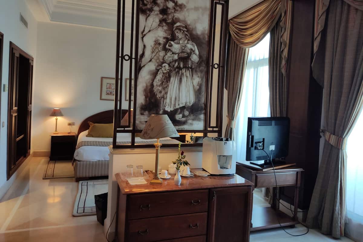 Quarto de hotel com cama, escrivaninha com computador, máquina de café, luminária, divisória decorativa e vista para o exterior.