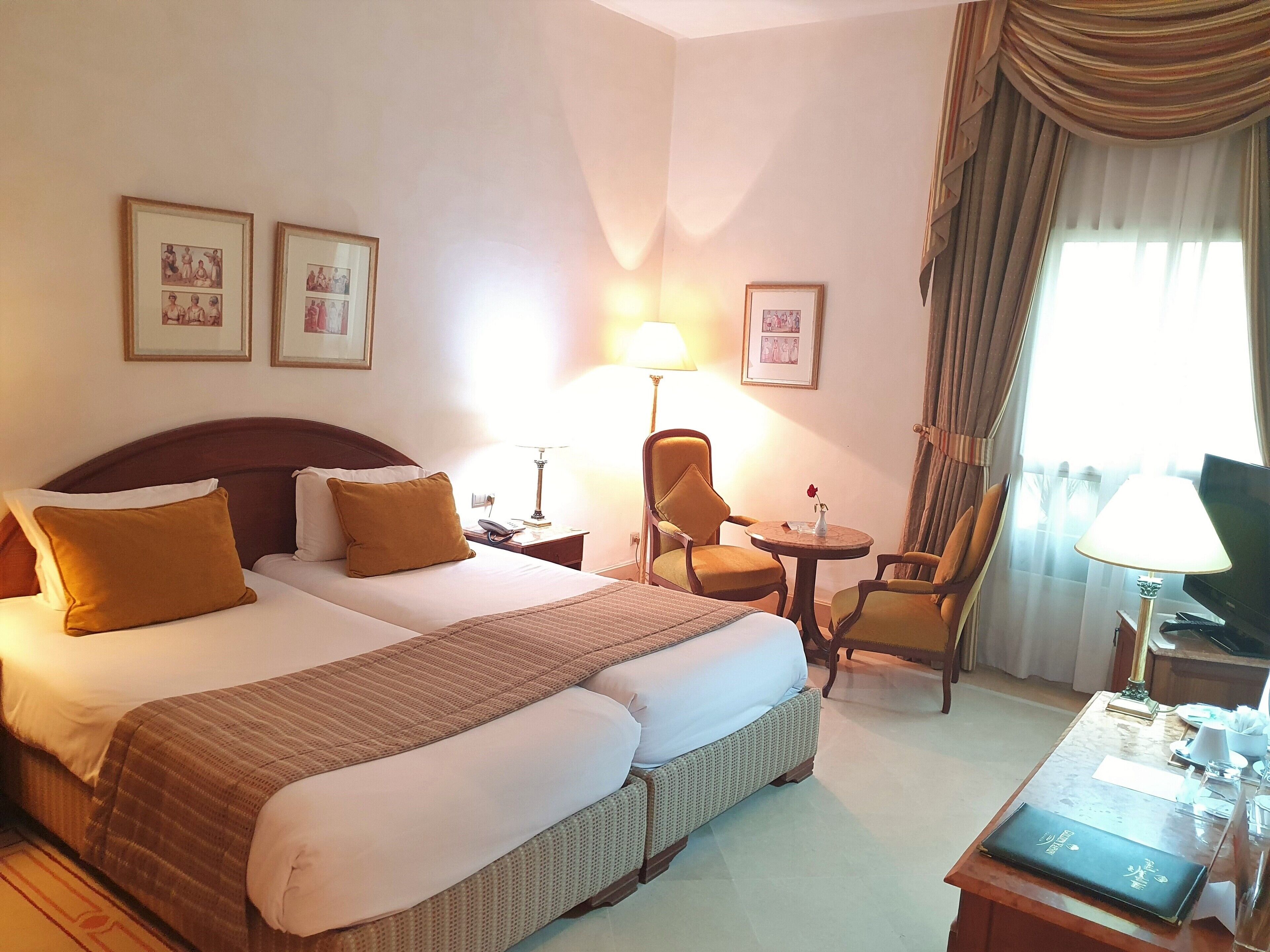A hotel room with a double bed, two armchairs, a small table, a TV, and framed pictures on the wall.