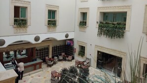Eine Hotelhalle mit mehreren Sitzbereichen, einem Empfangstisch und Zierpflanzen in Fensterkästen.