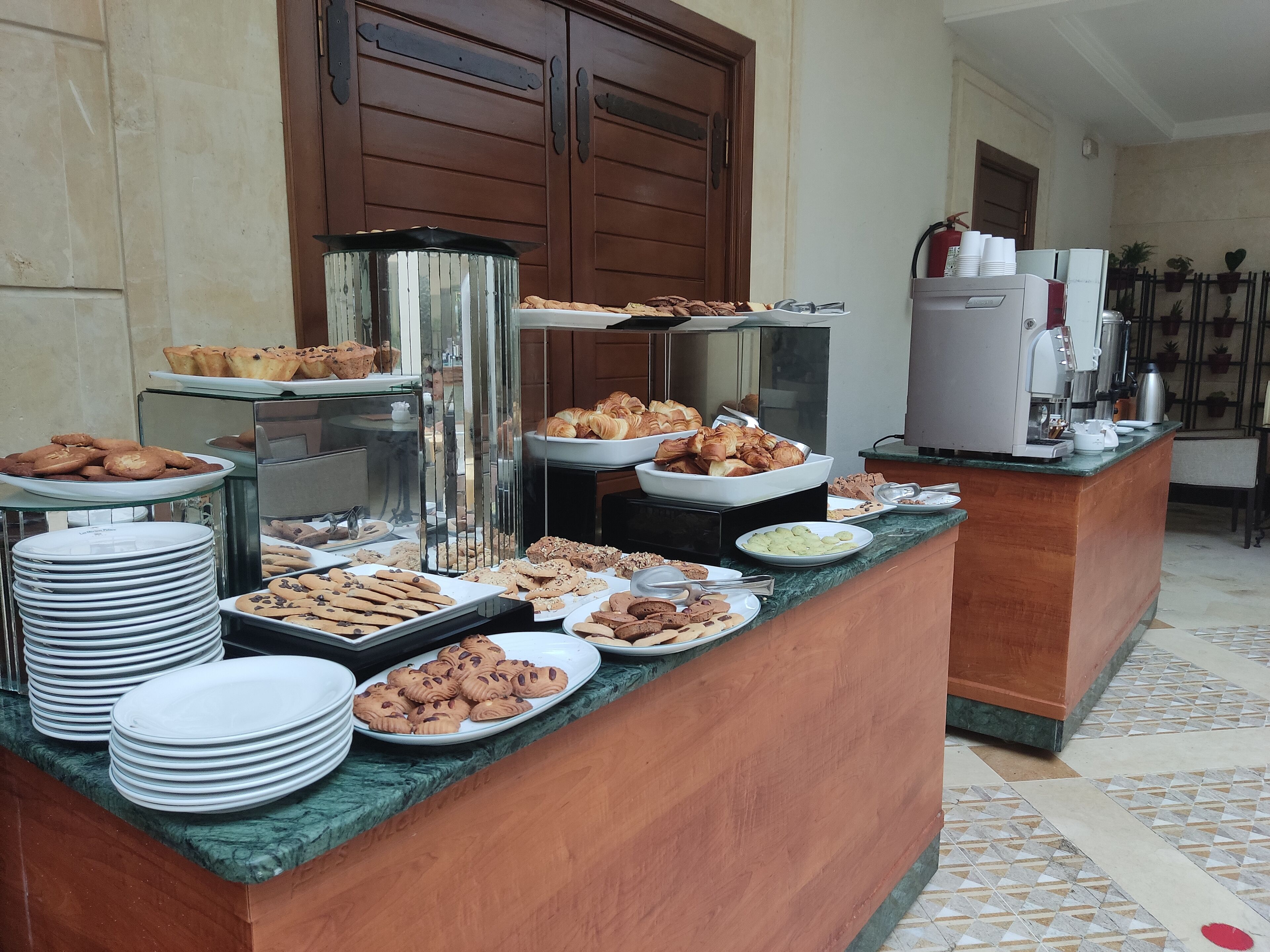 A buffet counter with various baked goods and pastries, a coffee machine, and a refrigerator.
