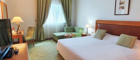 Een hotelkamer met een groot bed, een groene bank, een bureau met een lamp en een televisie.