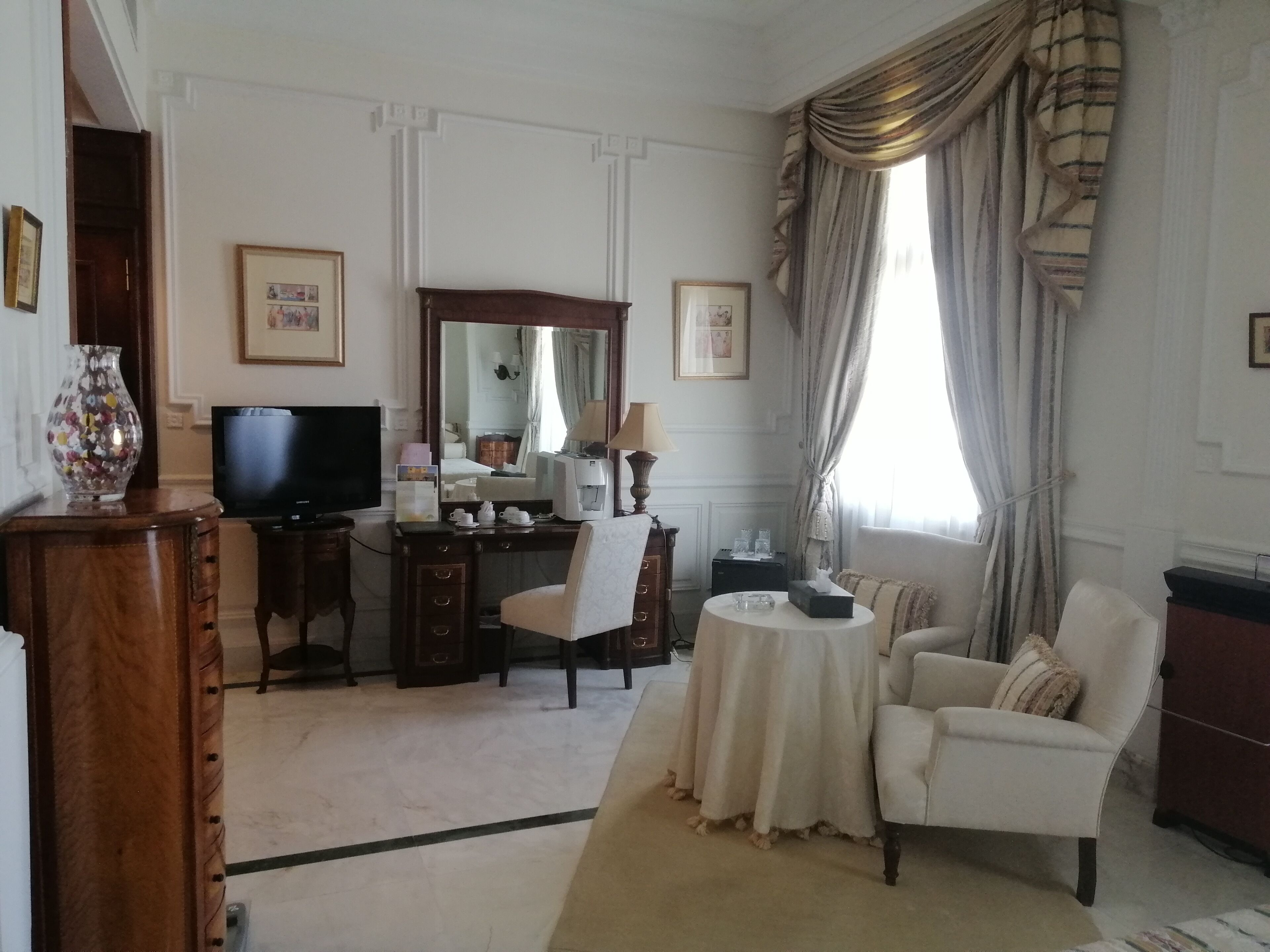 A hotel room with a wooden desk, a television, a mirror, a sofa, and a coffee table.