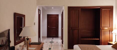 Habitación de hotel con cama, escritorio con lámpara, armario y puerta que da a otra habitación.
