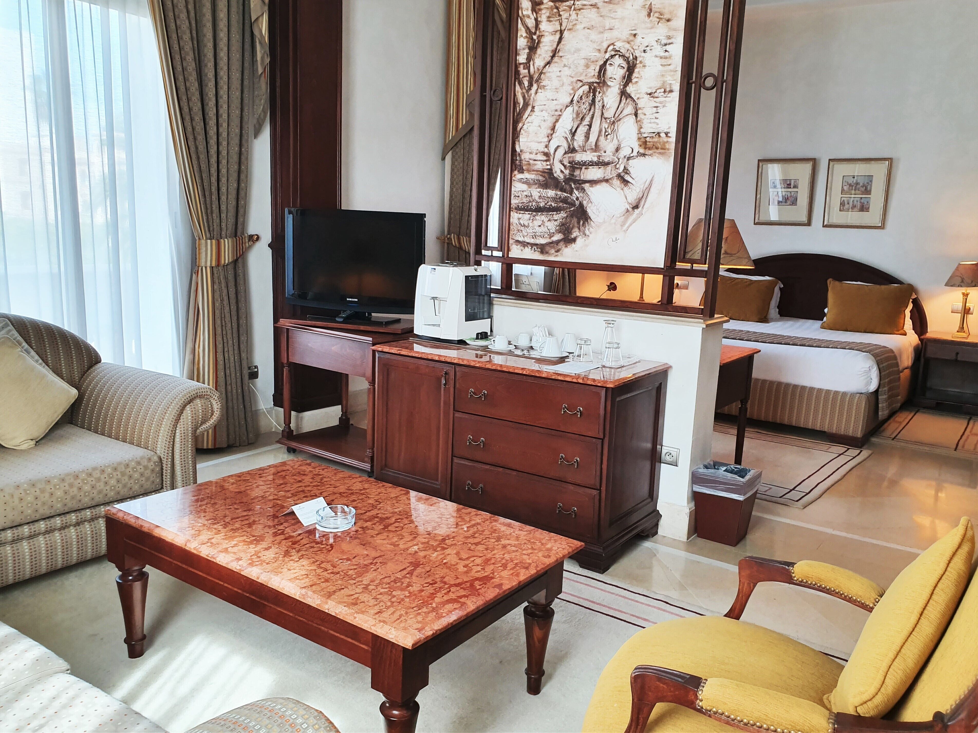 A hotel room with a TV, a desk with a computer, a bed, a sofa, and a chair.
