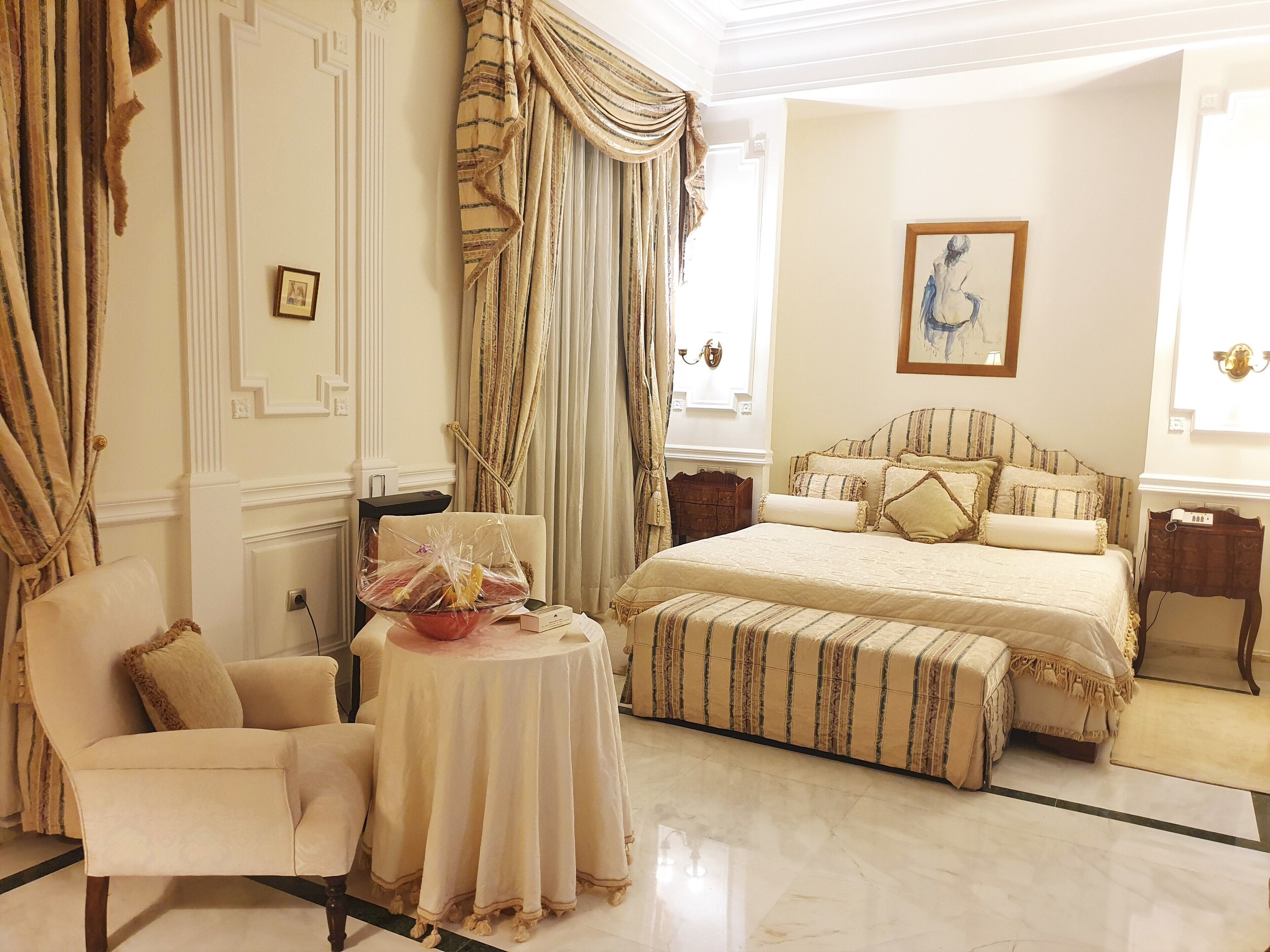 Une chambre bien aménagée, dotée d’un grand lit, d’un coin salon avec un fauteuil et une table, et d’une fenêtre avec des rideaux.