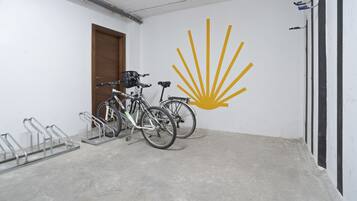 A room with a concrete floor, a wooden door, and a wall with a yellow sunburst logo. There are two bicycles parked against the wall.