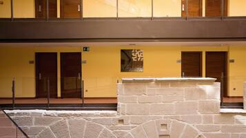 Un hotel de varios pisos con paredes amarillas, puertas numeradas y una fuente de piedra.