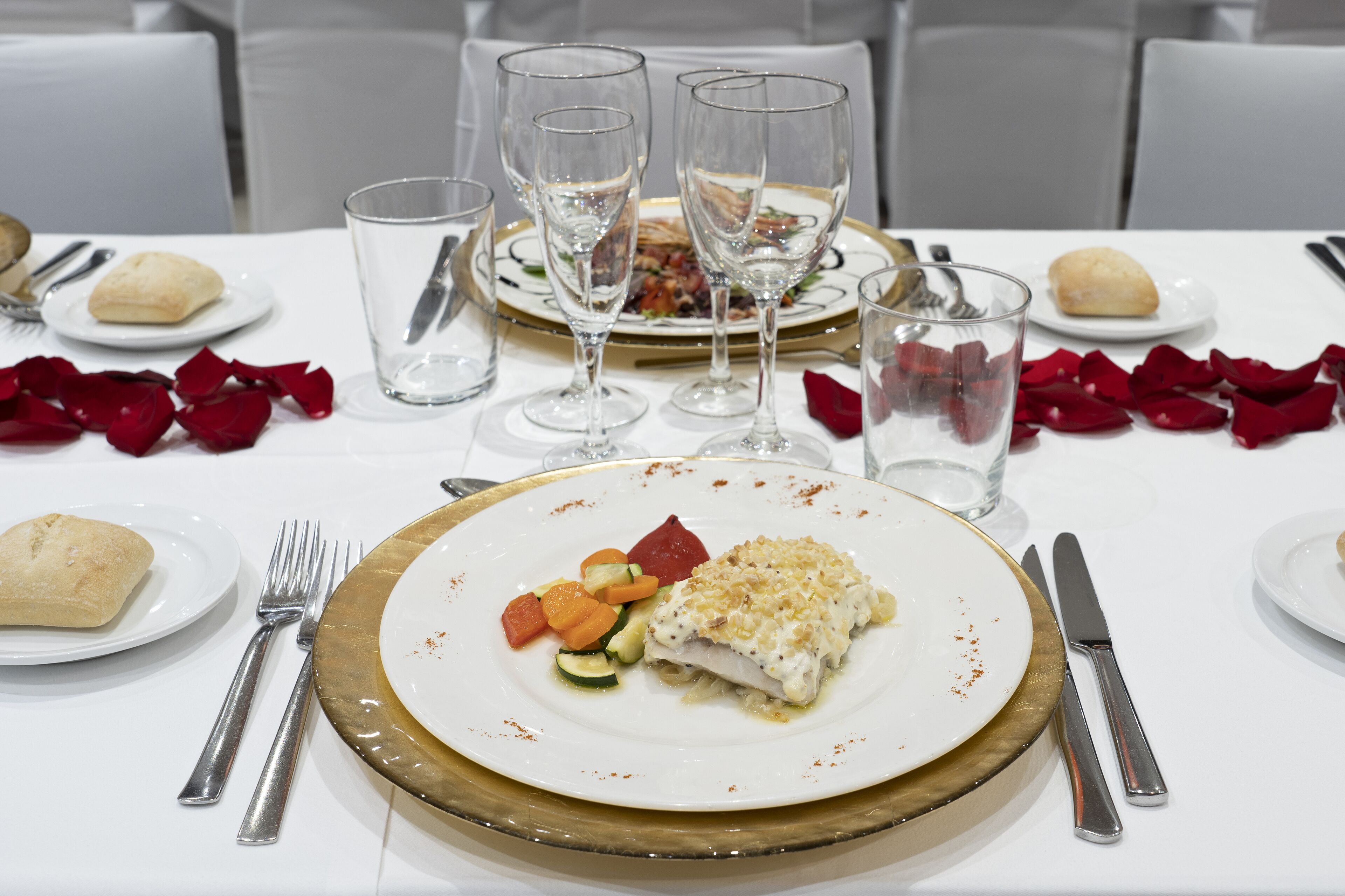 A dining table set with plates of food, wine glasses, and cutlery.