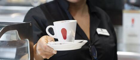 A person holding a white cup with a red heart design, wearing a black shirt with a name tag.