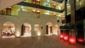 Un vestíbulo de hotel con piso de madera, arcos de piedra y un área de comedor al fondo.