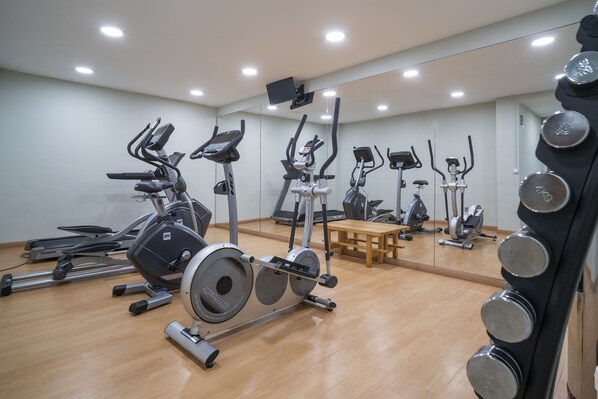 Un gimnasio con diferentes equipos de ejercicio, un espejo y una mesa de madera.