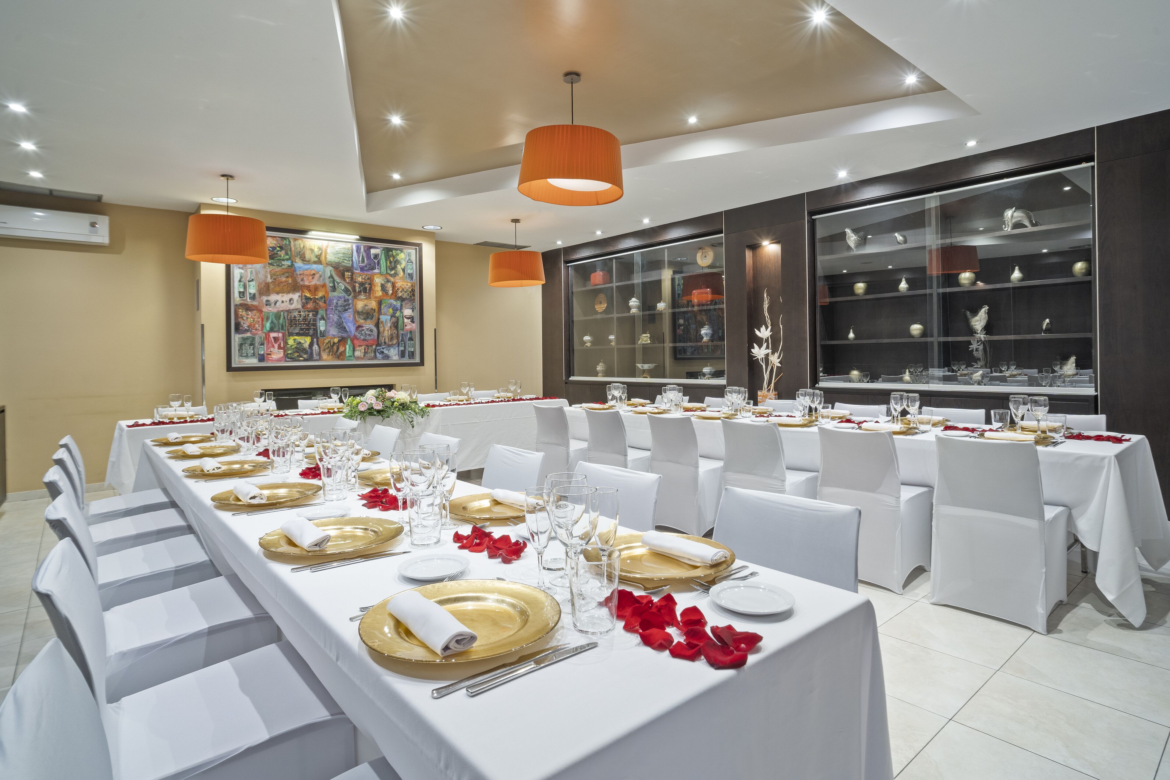 A banquet hall with long tables set for a formal event, white chairs, and a large decorative window display.