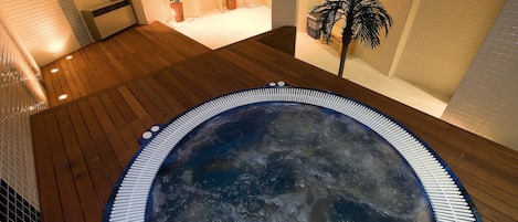 Un jacuzzi en un espacio interior bien iluminado, con piso de madera y paredes de azulejos.