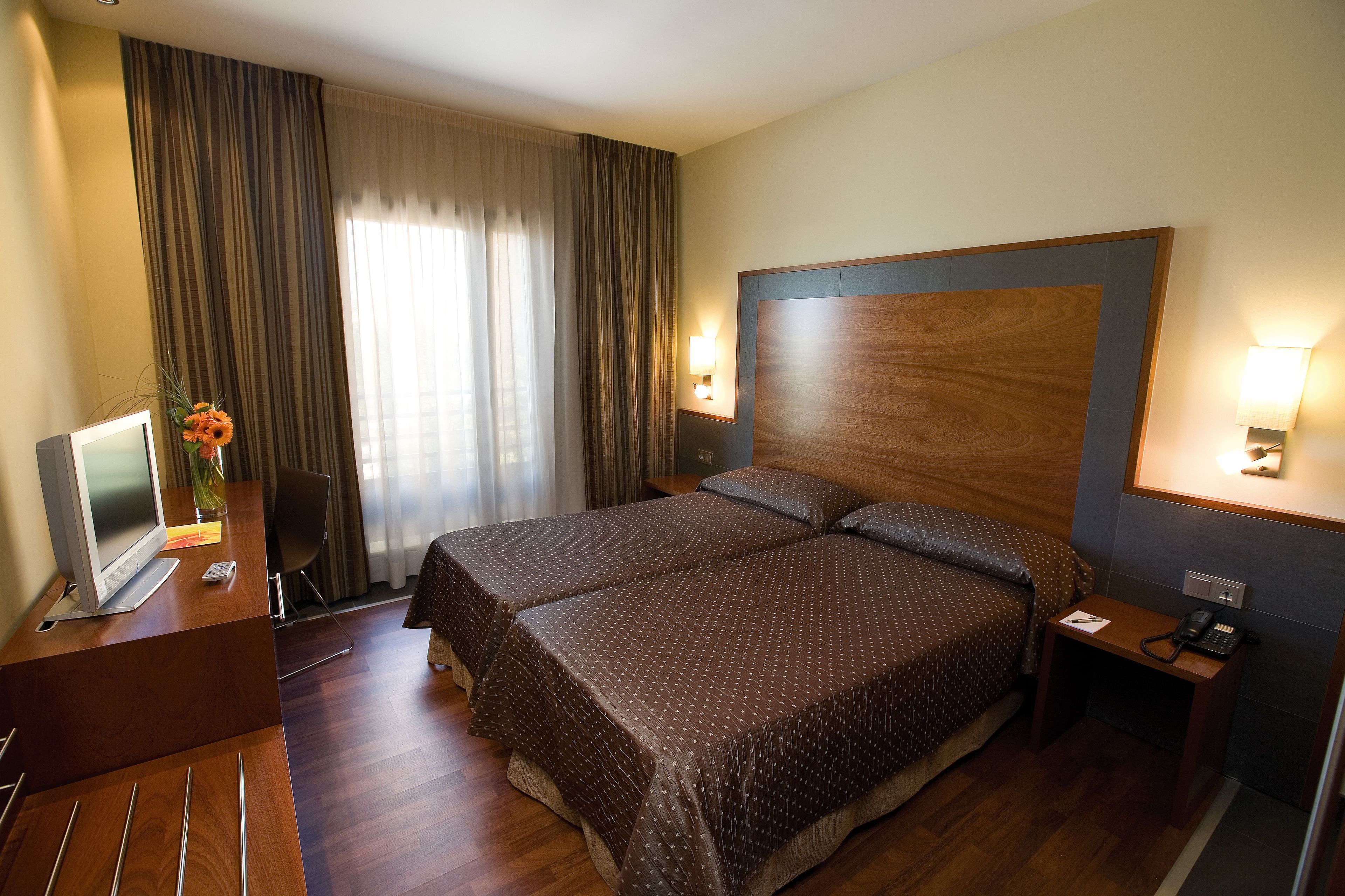 A hotel room with a large bed, a desk with a computer, a telephone, and a lamp.
