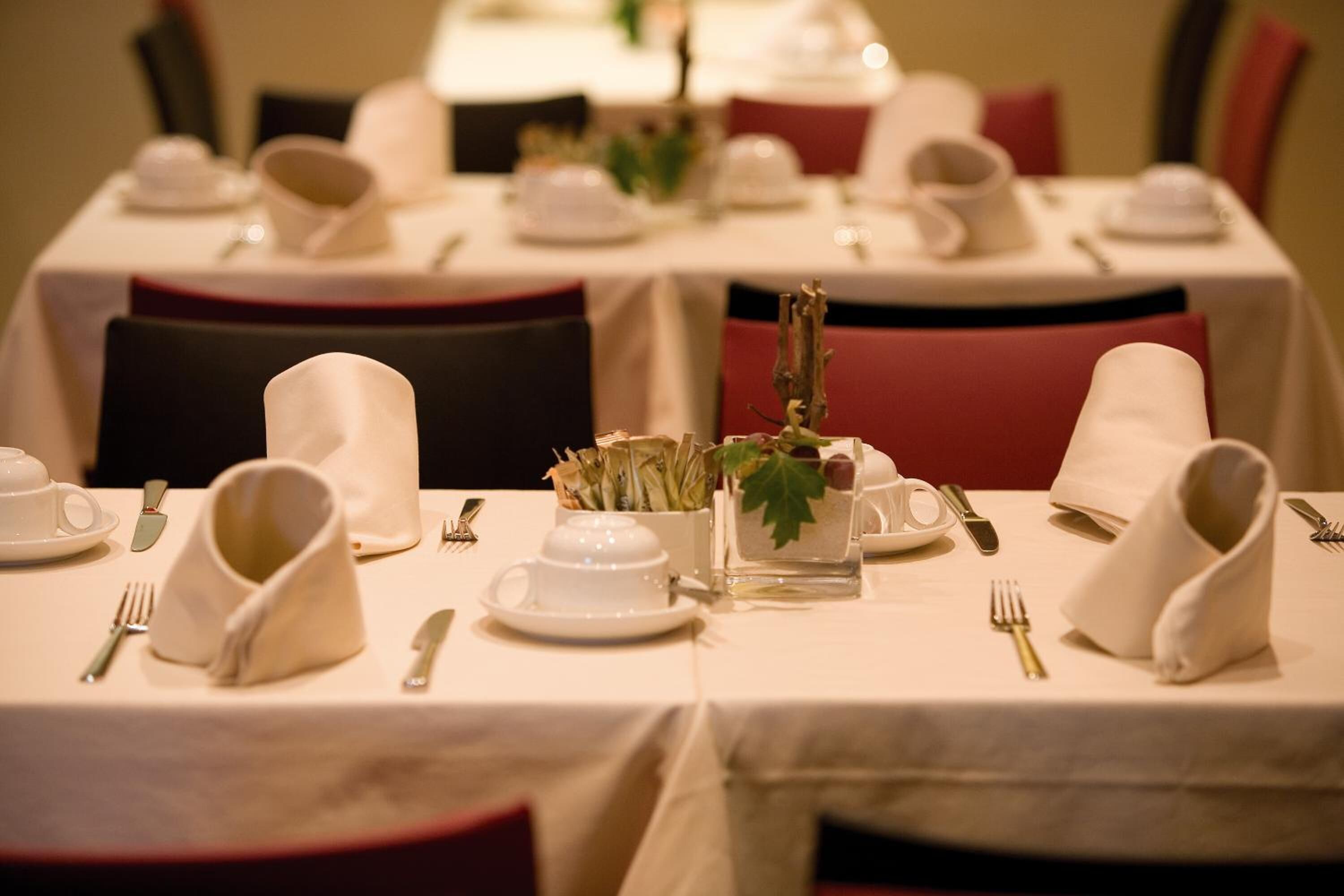 Une table à manger dressée avec de la vaisselle blanche, comprenant des assiettes, des tasses et des couverts, agrémentée d'un centre de table composé de verdure.
