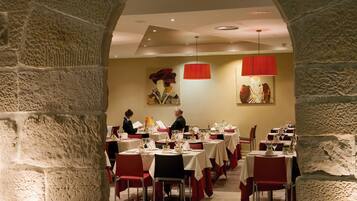 Un restaurante con paredes de piedra, sillas rojas y mesas dispuestas para comer.