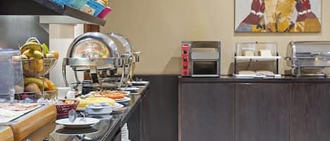 Una mesa de buffet con diversos alimentos, un microondas y un cuadro en la pared.