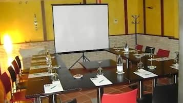 Una sala de conferències amb taula gran, cadires, pantalla de projector i paret de maó.