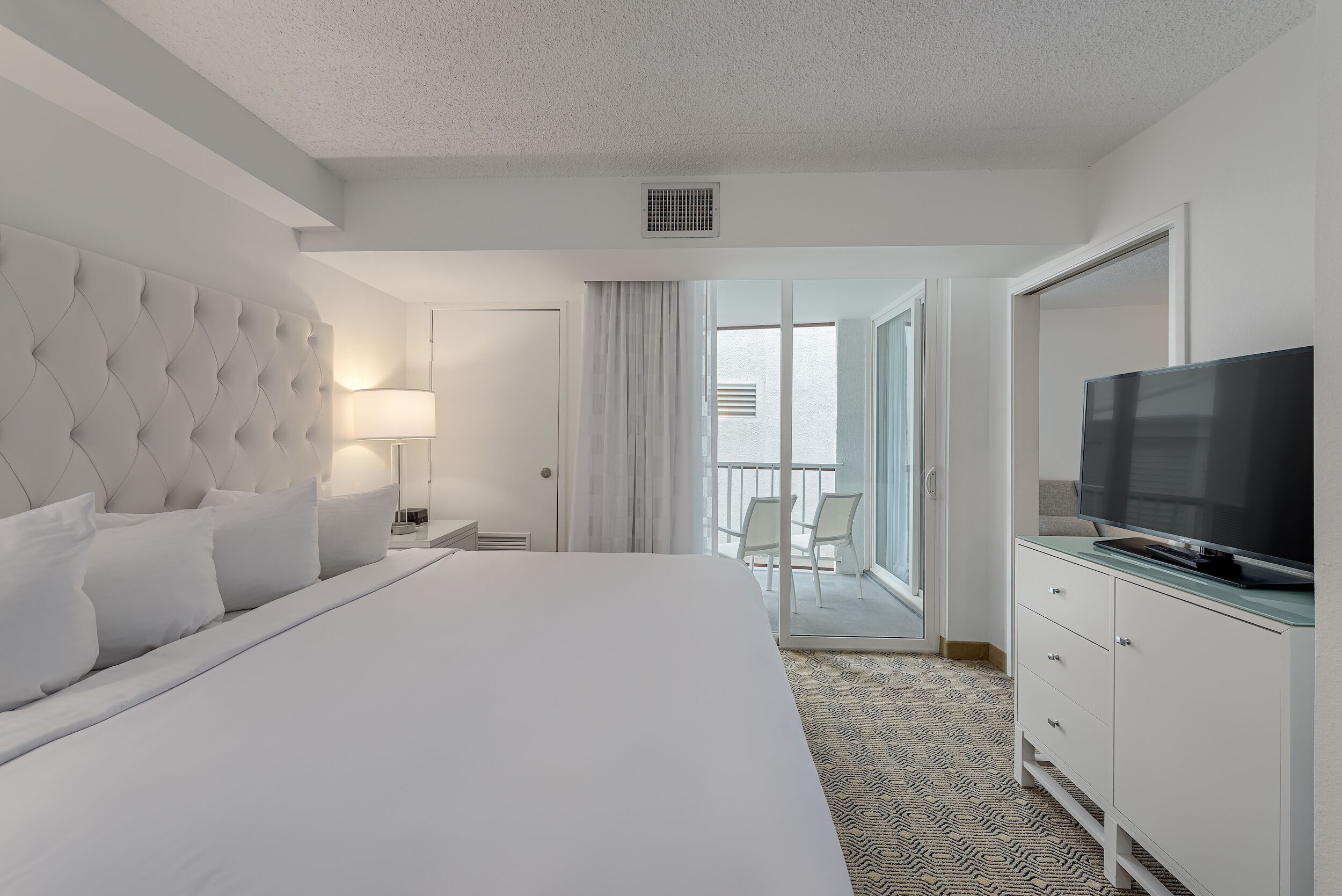 Ein Hotelzimmer mit einem großen Bett, einem Fernseher, einem Schminktisch und einem Balkon mit Aussicht.