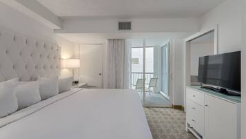 A hotel room with a large bed, a television, a dresser, and a balcony with a view.
