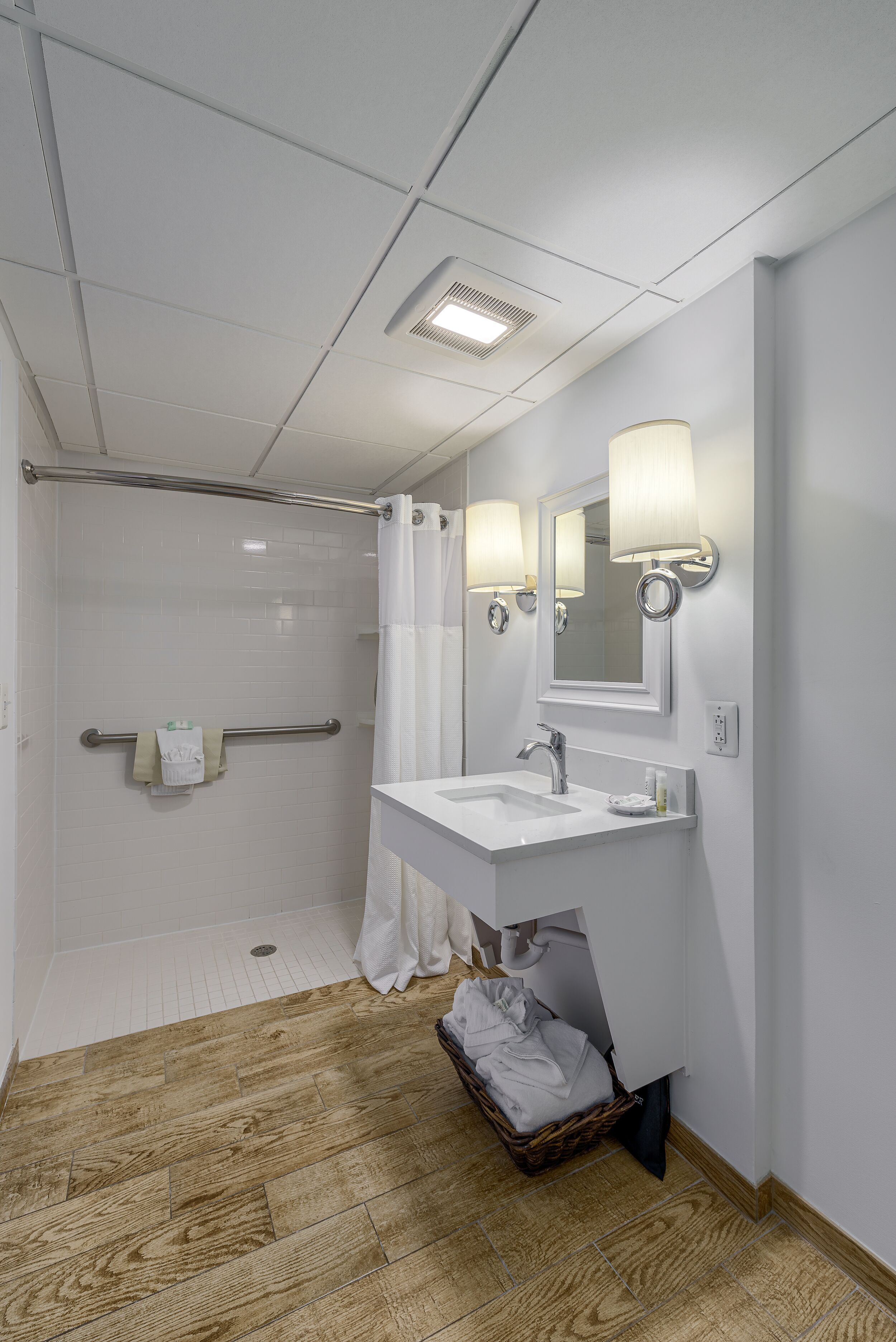 Un bagno d'hotel con doccia, lavandino e specchio illuminato da luci a parete.