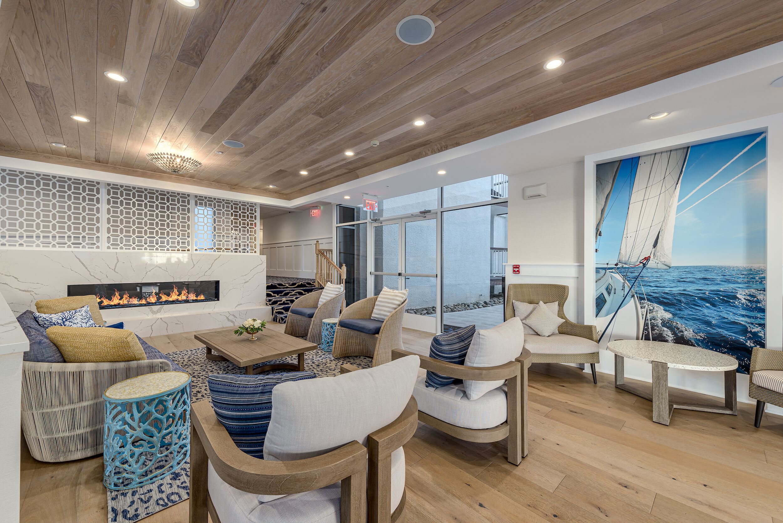 A spacious lounge area with wooden flooring, comfortable seating, a fireplace, and a large window offering a view of the sea.