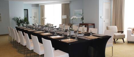 A conference room with a long table, white chairs, and a black tablecloth.
