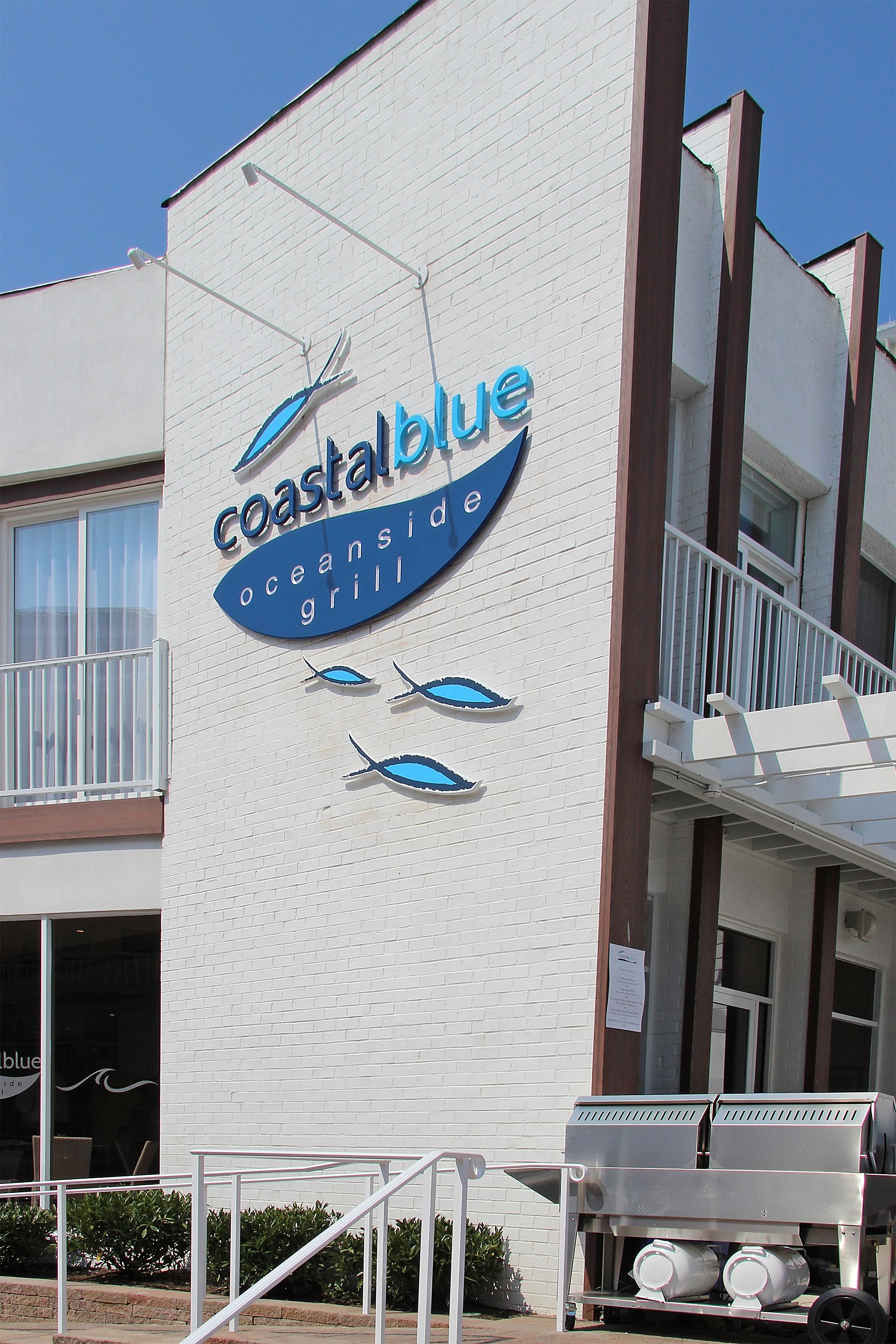 A building with a sign for 'Coastal Blue Oceanside Grill' featuring a fish graphic.
