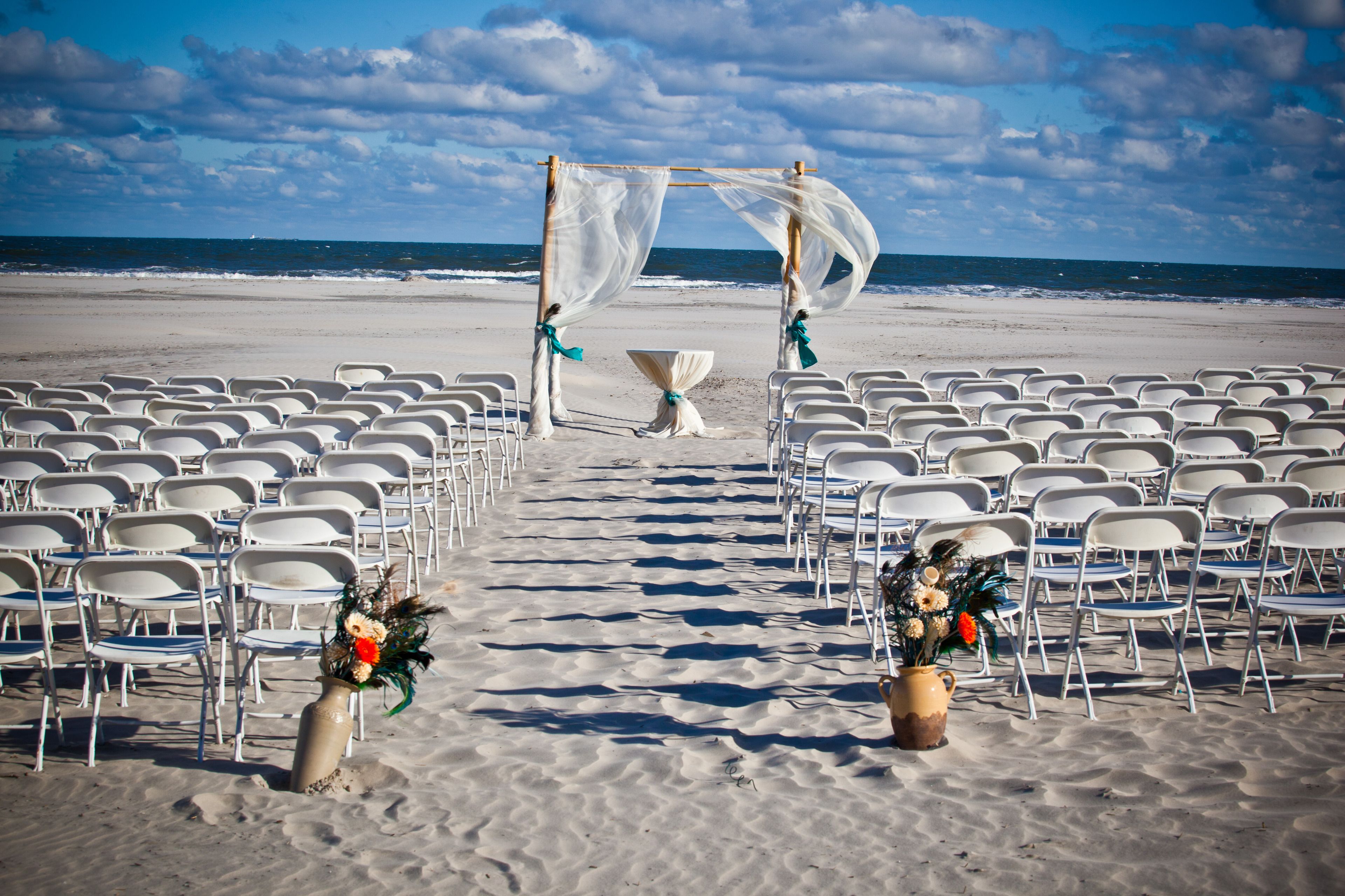 A beach wedding setup with chairs arranged in rows, a canopy, and floral centerpieces.